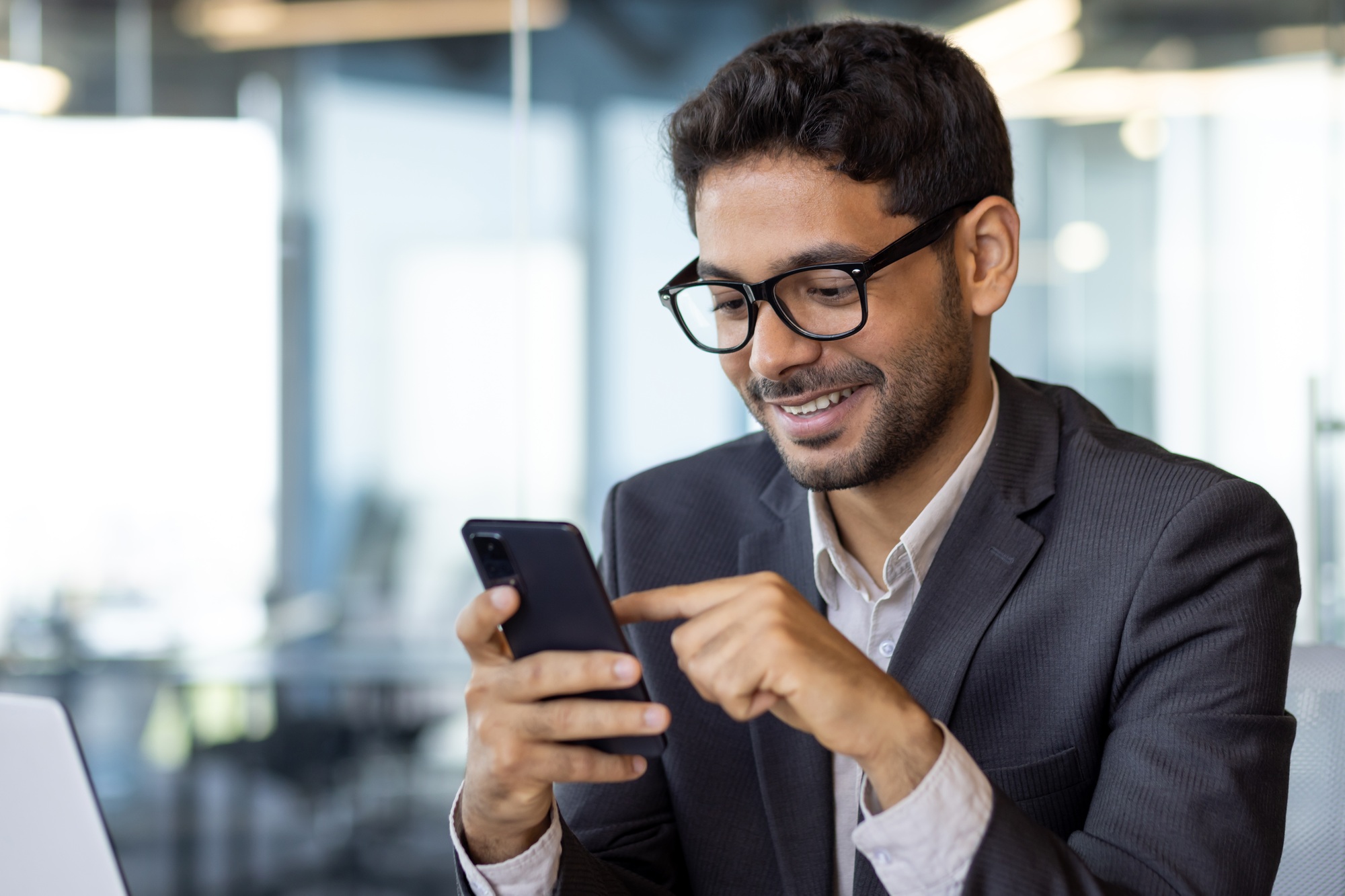 Successful experienced businessman using phone while sitting at workplace, hispanic smiling happy